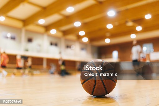 istock Basketball Training Game Background. Basketball on Wooden Court Floor Close Up with Blurred Players Playing Basketball Game in the Background 1427997649