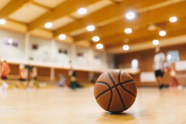 Photo of Basketball Training Game Background. Basketball on Wooden Court Floor Close Up with Blurred Players Playing Basketball Game in the Background