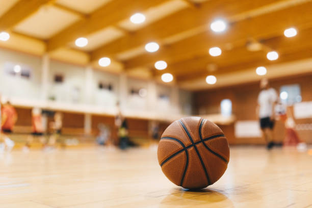 fundo do jogo de treinamento de basquete. basquete no piso da quadra de madeira fecha com jogadores borrados jogando basquete ao fundo - school gymnasium school basketball court gym - fotografias e filmes do acervo