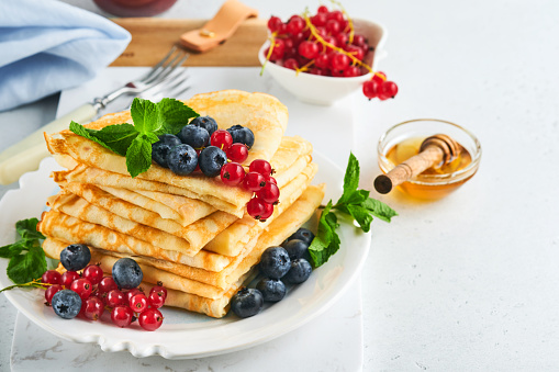 Pancakes. Stack of crepes or thin pancakes with berries, blueberries, red currants, raspberries and honey for breakfast. Homemade breakfast. Copy space. Selective focus.