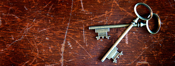 On an old book with clasps, there is an old key made of metal. Antique objects on a dark wooden background.