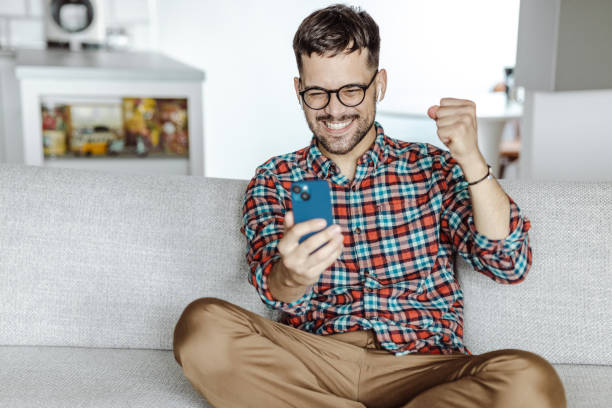 istock A smiling man holding a mobile phone and celebrating success 1428001570