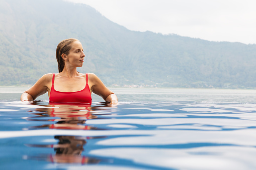 Young woman relax in infinity pool with lake view. Natural hot spring spa under Batur volcano. Travel in Kintamani, Bali. Healthy lifestyle, recreational activity on family summer holiday.
