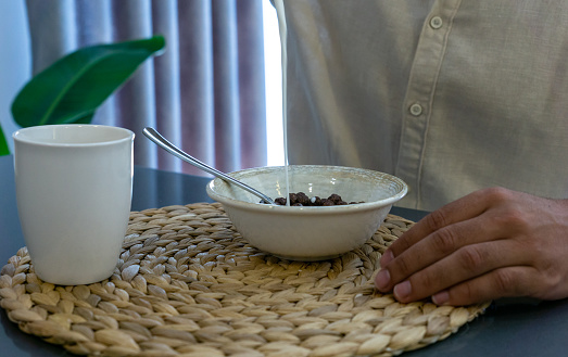 Close-up of unrecognizable man pouring milk and eating cereal for breakfast.