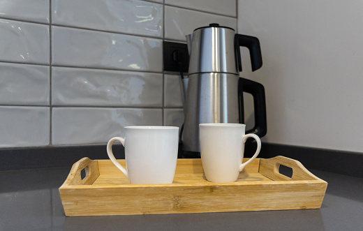 Electric kettle with a wooden tray with two white cups in the kitchen