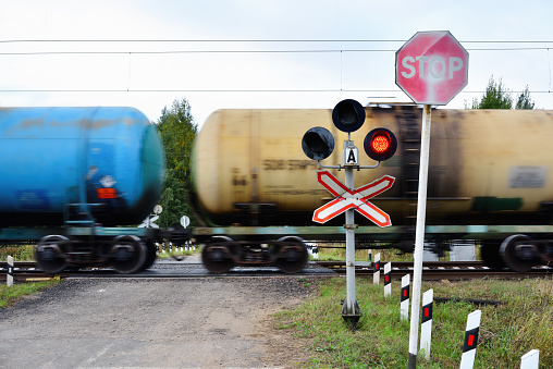 Russia, Vologda region, Kholmische village - September 18, 2022. Stop sign in front of a railroad crossing. A passing train in front of a closed railroad crossing. Road signs.