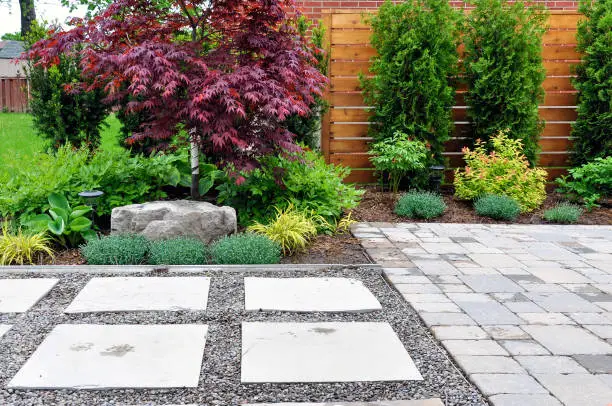 Photo of Hardscape details of a tumbled paver patio, flagstone stepping stones and horizontal cedar fence in a modern Japanese garden.