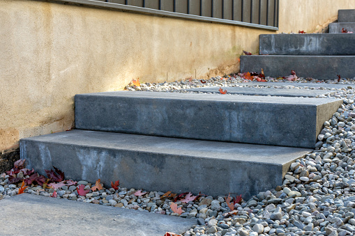 Grey precast concrete steps with matching stepping stone slabs and river rock run along the side of a home, providing a safe transition to sideyard to the backyard below.