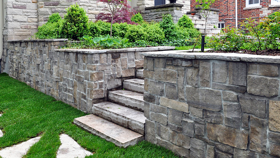 Luxury landscaping shows natural stone steps, a retaining wall with coping, and oversized flagstone stepping stones.