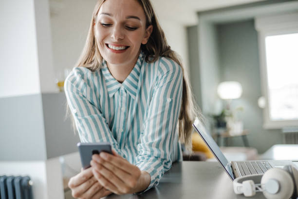 istock Blond hair woman using mobile phone at home and smiling 1428037556