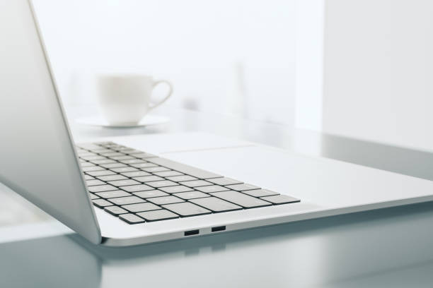 istock Close up of modern laptop side view with white coffee cup on light table with abstract reflection. 3D rendering 1428038322