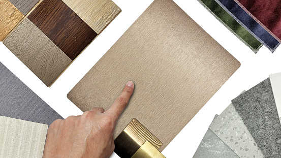 interior architect's hand choosing furnishing material samples consists copper laminated, gold aluminums, artificial stones, wooden engineering floorings, drapery fabrics, interior wallpapers