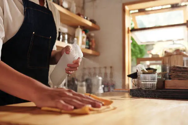 Closeup image of coffeeshop owner sparying detergent on counter and wiping with soft cloth