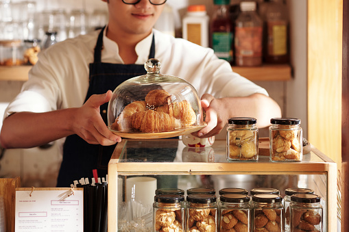 Cropped image of cafe waiter putting plate with fresh croissants on counter to sell