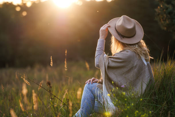 Carefree woman with hat and poncho relaxing outdoors during sunset Happy woman with hat and poncho relaxing outdoors during sunset. Mental wellbeing and resting in nature indian summer stock pictures, royalty-free photos & images