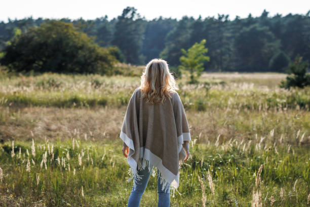 Blond hair woman with beige poncho standing in nature Boho woman with poncho standing outdoors. Enjoyment of spending time in nature indian summer stock pictures, royalty-free photos & images