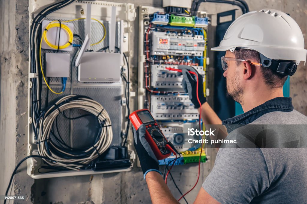 Man, an electrical technician working in a switchboard with fuses. Man, an electrical technician working in a switchboard with fuses. Installation and connection of electrical equipment. Professional uses a tablet. Electrician Stock Photo