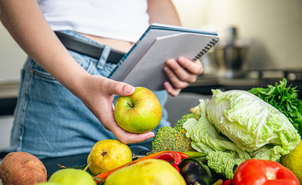 femme avec bloc-notes et légumes sur la table de la cuisine préparant une recette. - cabbage palm photos et images de collection