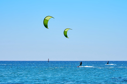 Rhodes, Greece - July 10 2017: Strong sportsmens goes kitesurfing on tranquil azure sea water against clear blue sky on sunny summer day at tropical resort