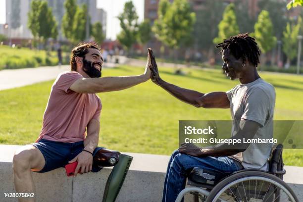 Two Disabled Friends One Hispanic With An Amputated Leg Prosthesis The Other African In A Wheelchair Highfives As A Sign Of Friendship Concept Of Strength And Overcoming Difficulties Stock Photo - Download Image Now