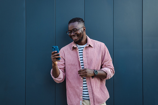 Shot of a young smiling man using a smart phone and surfing the net. He is standing in front grey background