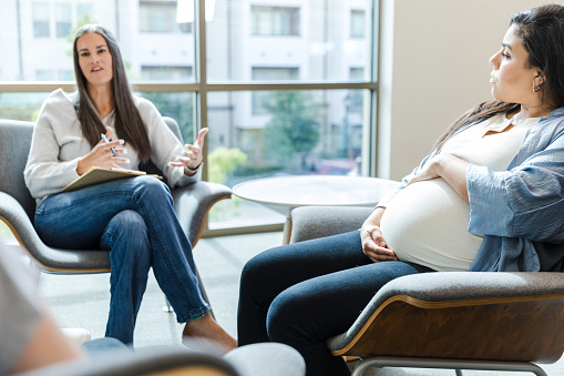 The young adult expectant mom listens to the advice of the female counselor during group therapy.