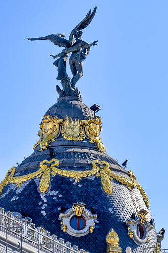 Madrid, Spain - September 15, 2022: View of a large ornate dome on a building. There is a statue of a two-winged creature on the dome.