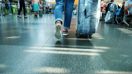 close-up. back view. female legs in sneakers. Woman, Traveler, passenger with her wrapped suitcase, luggage walking through the hall of Airport. High quality photo