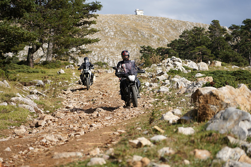 Two man riding an off-road motorcycle on a mountain road