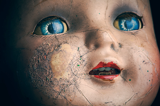 A macro shot of a cracked and dirty creepy old baby doll's face.