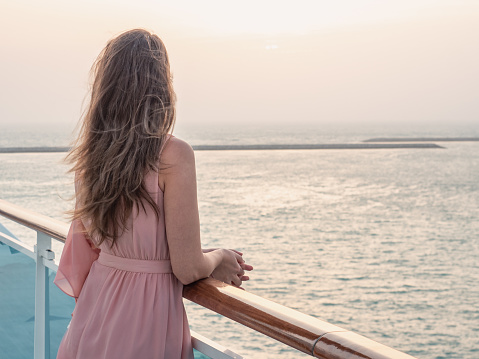 Beautiful woman standing on the empty deck of a cruise liner against the backdrop of the setting sun. Closeup, outdoor. Vacation and travel concept