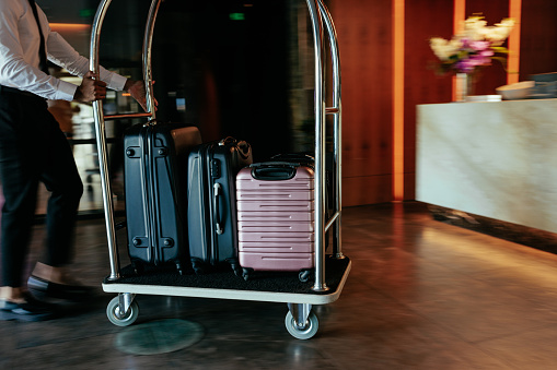 A young bellhop is pushing the luggage cart across the hotel lobby filled with suitcases.