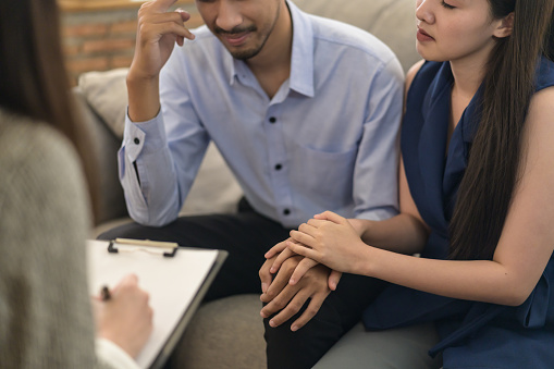 Healthcare concept: Young Asian couple received a consultant with professional psychologist doctor in psychotherapy session or counsel diagnosis health. Wife encourage her husband during psychotherapy