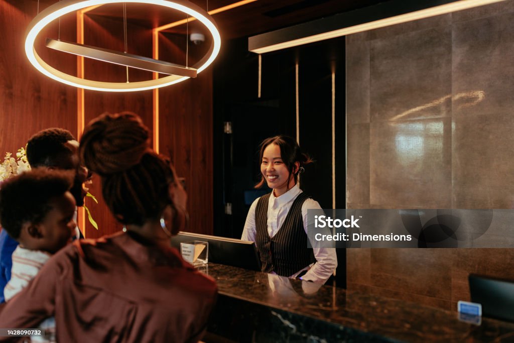Happy receptionist talking to hotel guests. A young Asian receptionist is at the front desk of a luxurious hotel talking to her African American hotel guests. Hotel Stock Photo