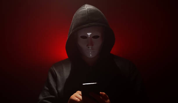 Man wearing mask with hoodie launches virus from smartphone. Man wearing mask with hoodie launches virus from smartphone. vendetta stock pictures, royalty-free photos & images