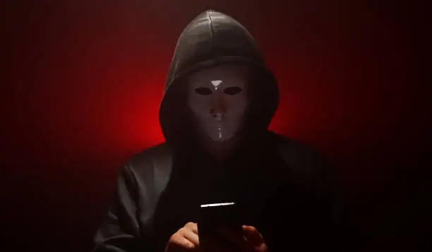 Man wearing mask with hoodie launches virus from smartphone.