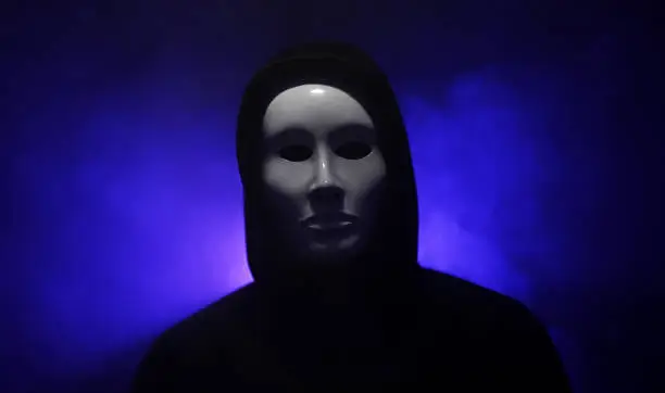 Man wearing mask with hoodie on blue background.
