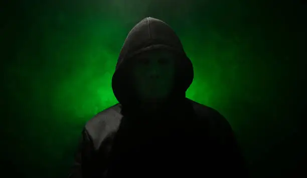 Man wearing mask with hoodie on green background.