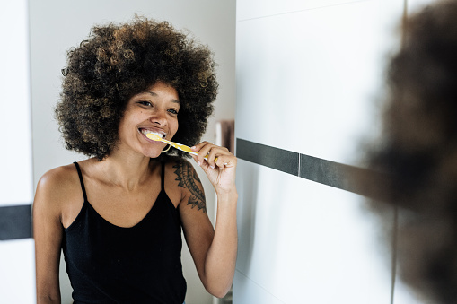 Multiracial woman brushing teeth in bathroom in front of the mirror