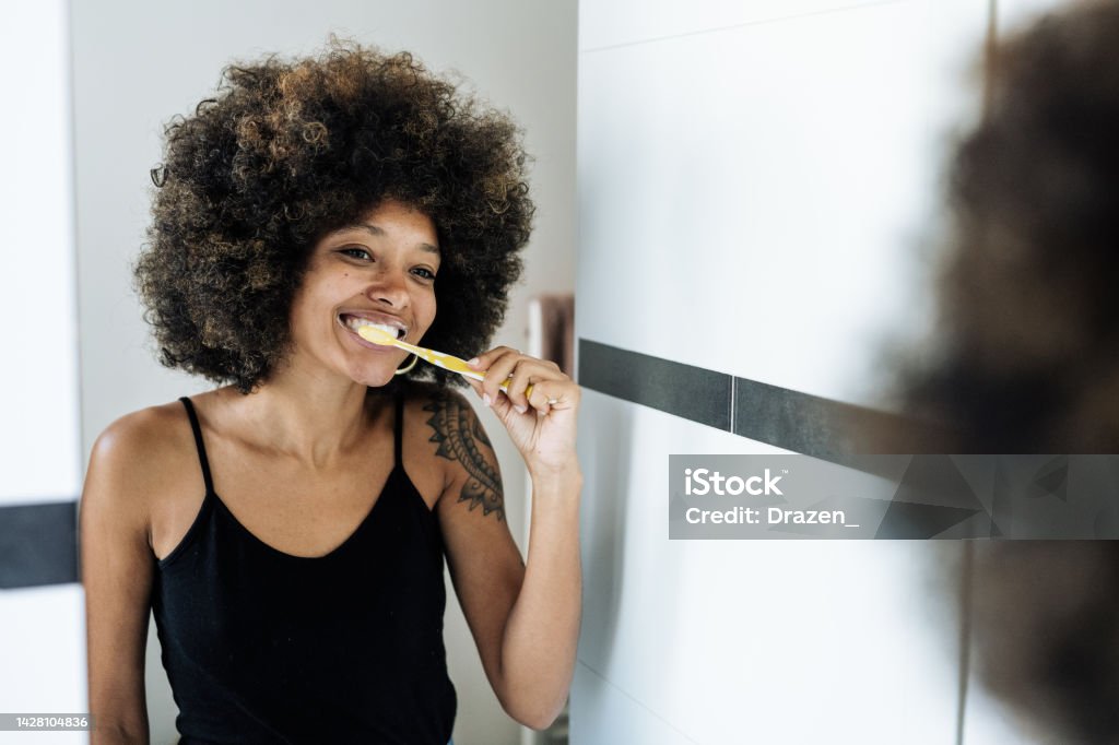 Multiracial woman brushing teeth in bathroom in front of the mirror Brushing Teeth Stock Photo