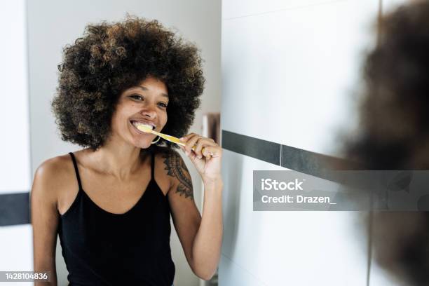Multiracial Woman Brushing Teeth In Bathroom In Front Of The Mirror Stock Photo - Download Image Now