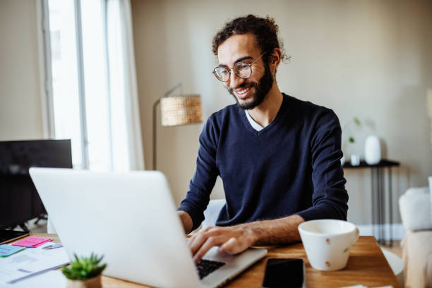 istock Modern multiracial man working from home, using laptop in living room and business document for online business meeting 1428106066