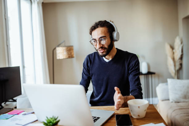 istock Modern multiracial man working from home, using laptop in living room and business document for online business meeting 1428106117