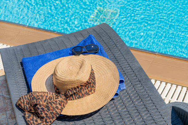 A womans sun hat and towel on a sun lounger beside a swimming pool