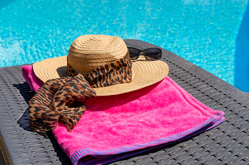 A womans sun hat and towel on a sun lounger beside a swimming pool