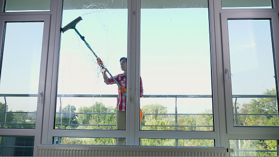 smiling Caucasian Beautiful woman, housewife or Cheerful female worker of cleaning service, in gloves, Cleaning, washing Windows by special mop, enjoying her work. Cleaning lady. High quality photo