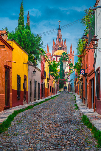 Show casing Mexican style architecture and culture with colorful buildings on the cobblestone streets of San Miguel de Allende Mexico with the iconic Church of St Michael in the background.