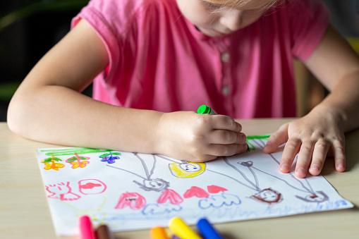 Child drawing a picture of her family with colored markers. Little girl, sitting at the table.