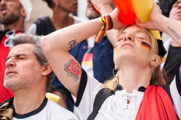 Disappointed German football fan holding her head next to frustrated German man at Germany national team game Mid-shot of disappointed German football fan holding her head next to frustrated German man at Germany national team game in crowded stadium women under 20 stock pictures, royalty-free photos & images