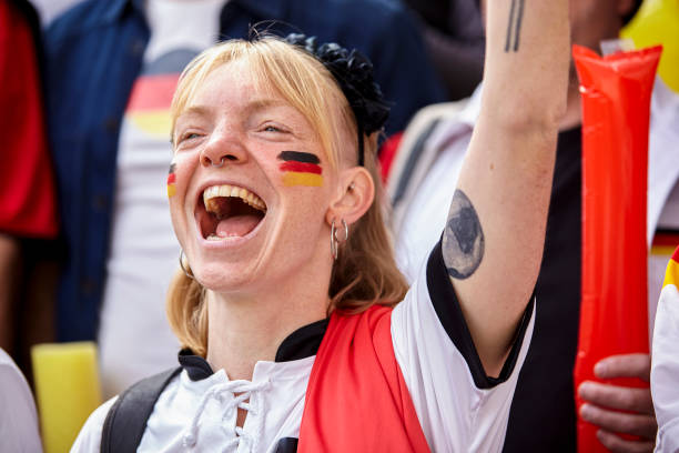 Happy German football fan chanting and cheering with one arm in the air at Germany national team match Mid-shot of happy German football fan chanting and cheering with one arm in the air in crowded stadium at Germany national team international match women under 20 stock pictures, royalty-free photos & images